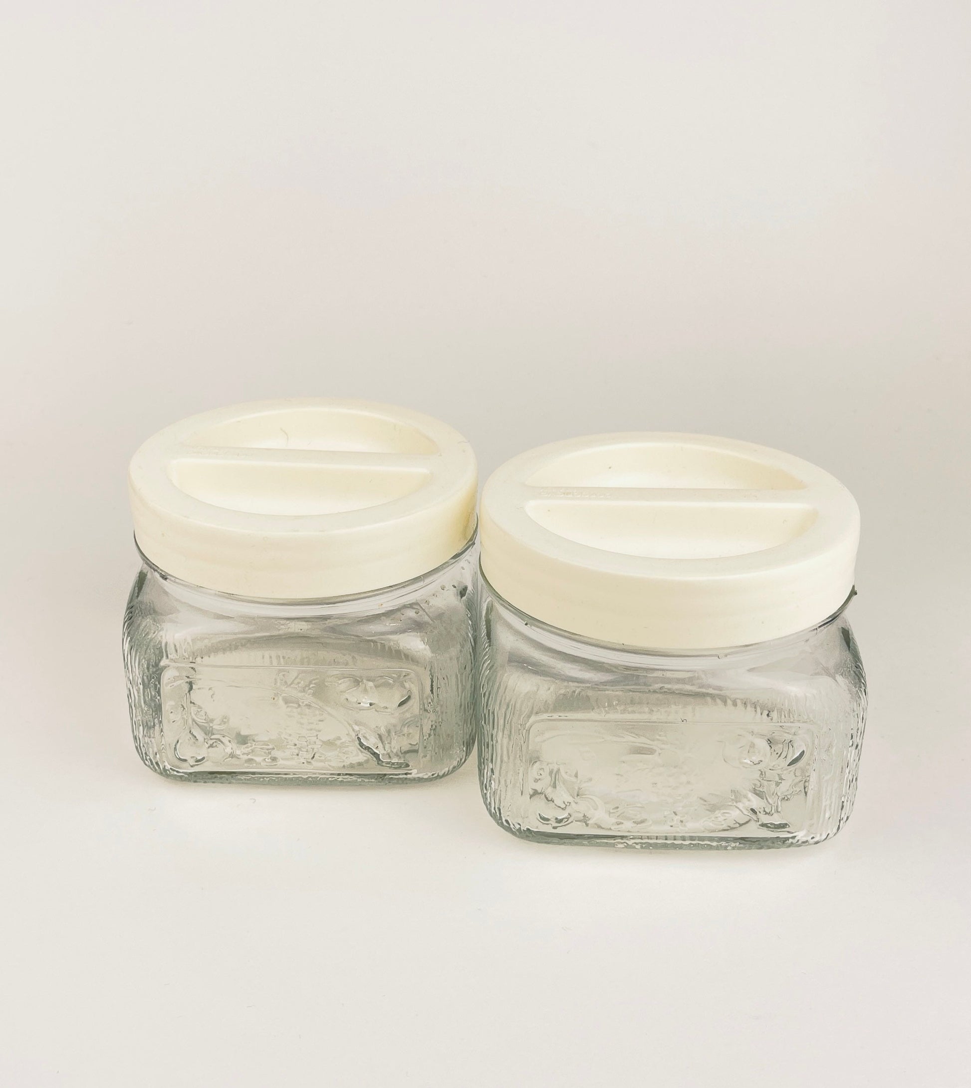 Two clear glass jars with white lids on a light gray background