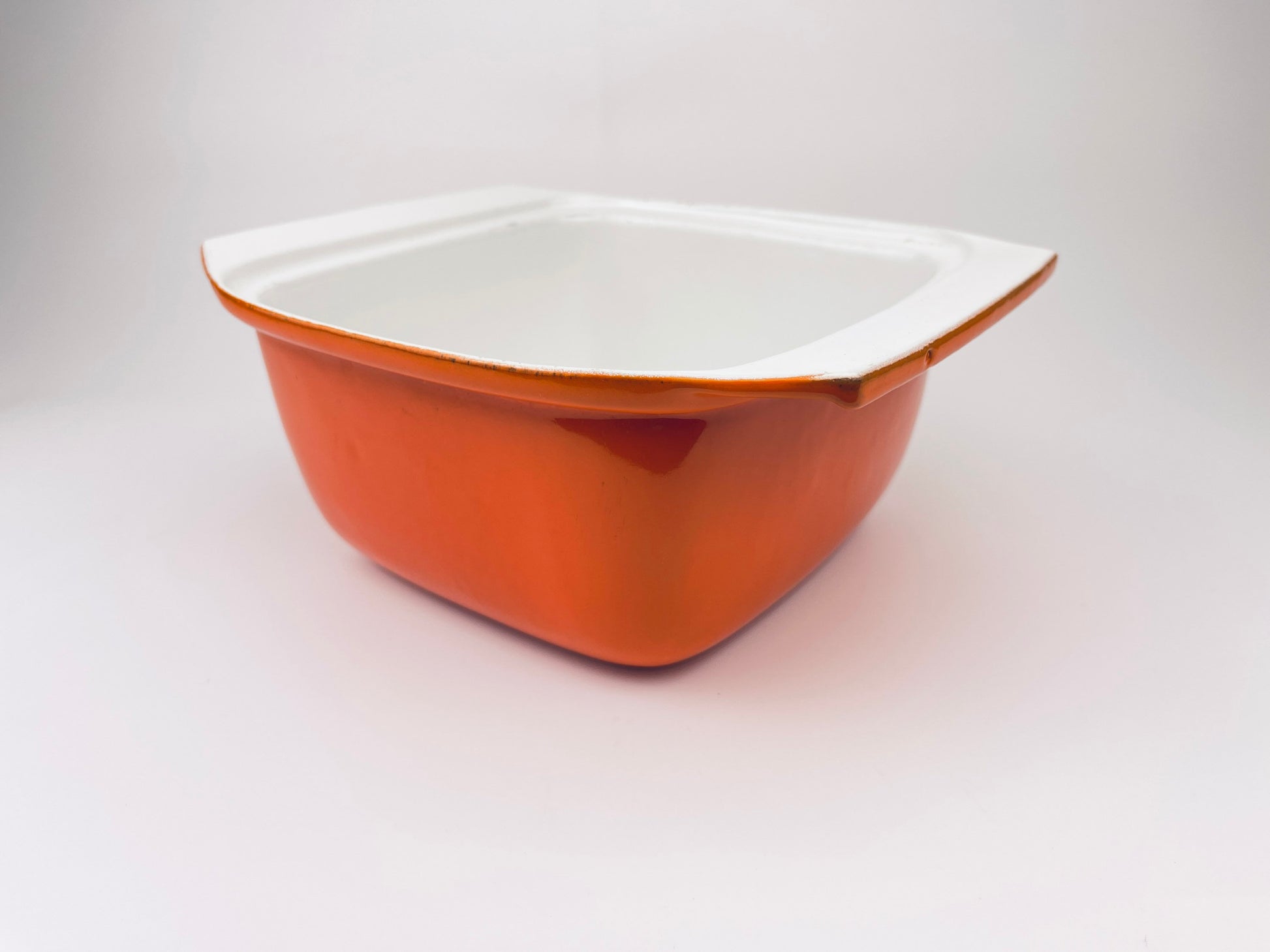 Orange ceramic coated cast iron pot with white interior on a light gray background