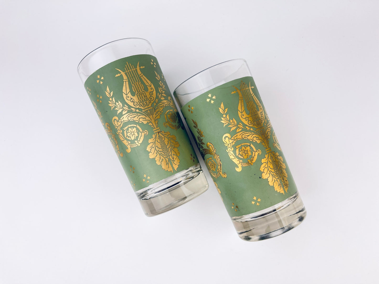 Two green glasses with gold decorative patterns on a white background