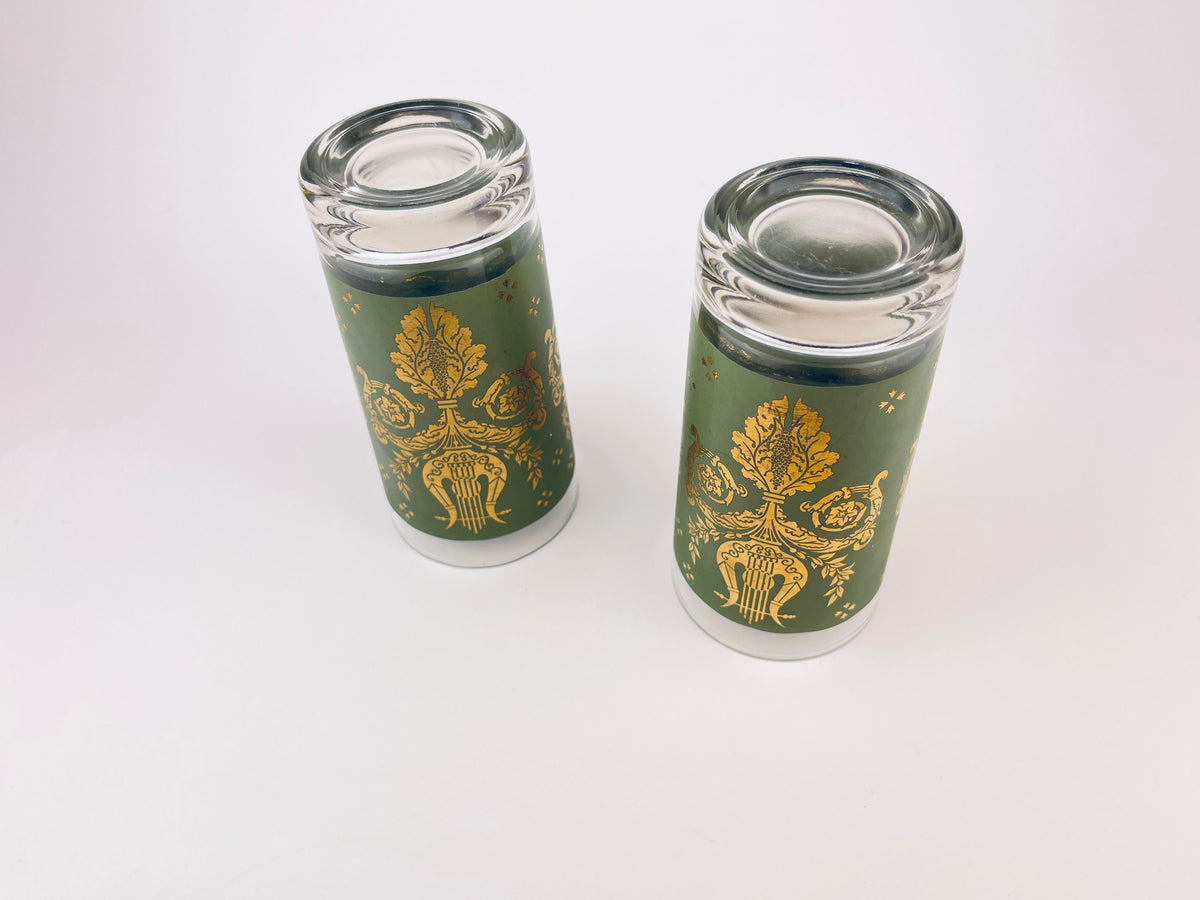 Two green glass tumblers with gold designs on a white background