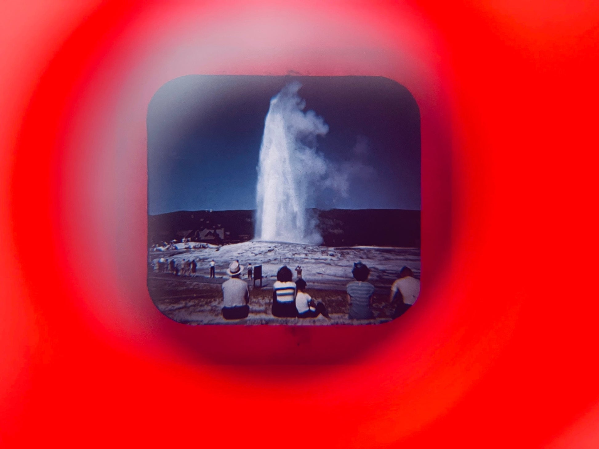 People watching a geyser erupt with a red circular frame overlay