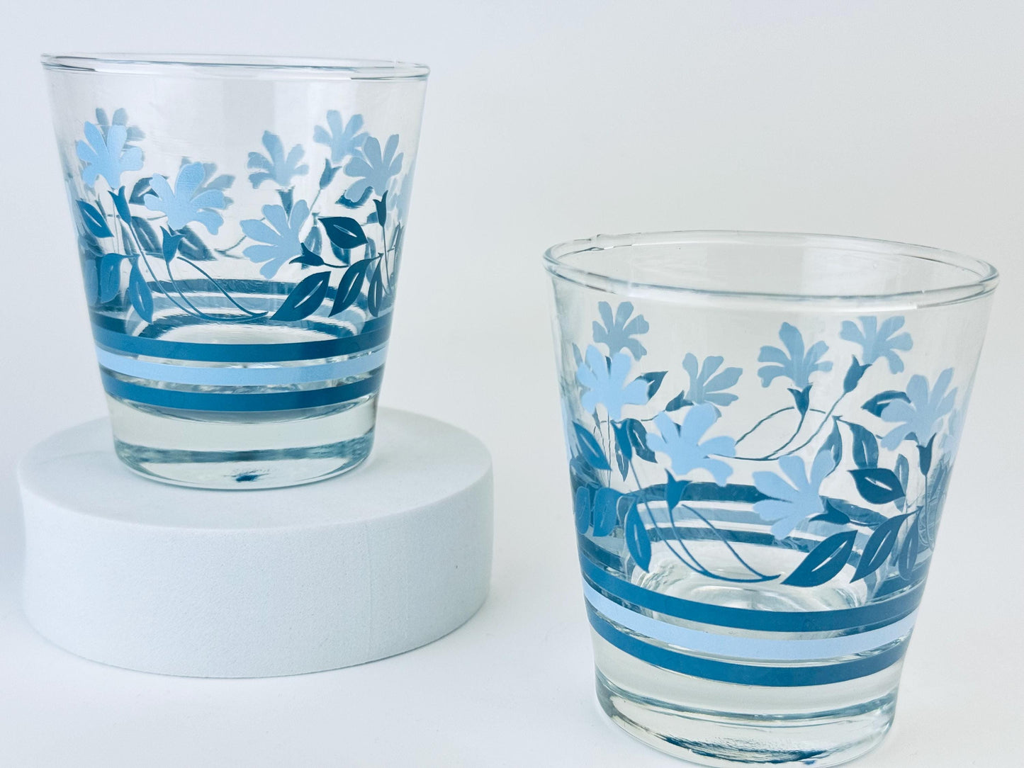 Pair of vintage 1970s blue floral glass juice tumblers with pressed floral pattern on white background.