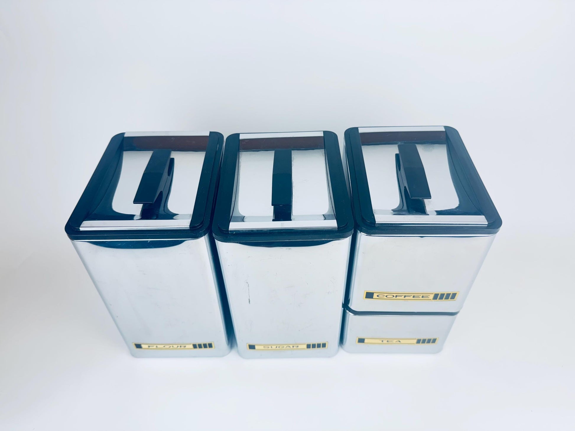 Four metal coffee canisters with lids on a white background