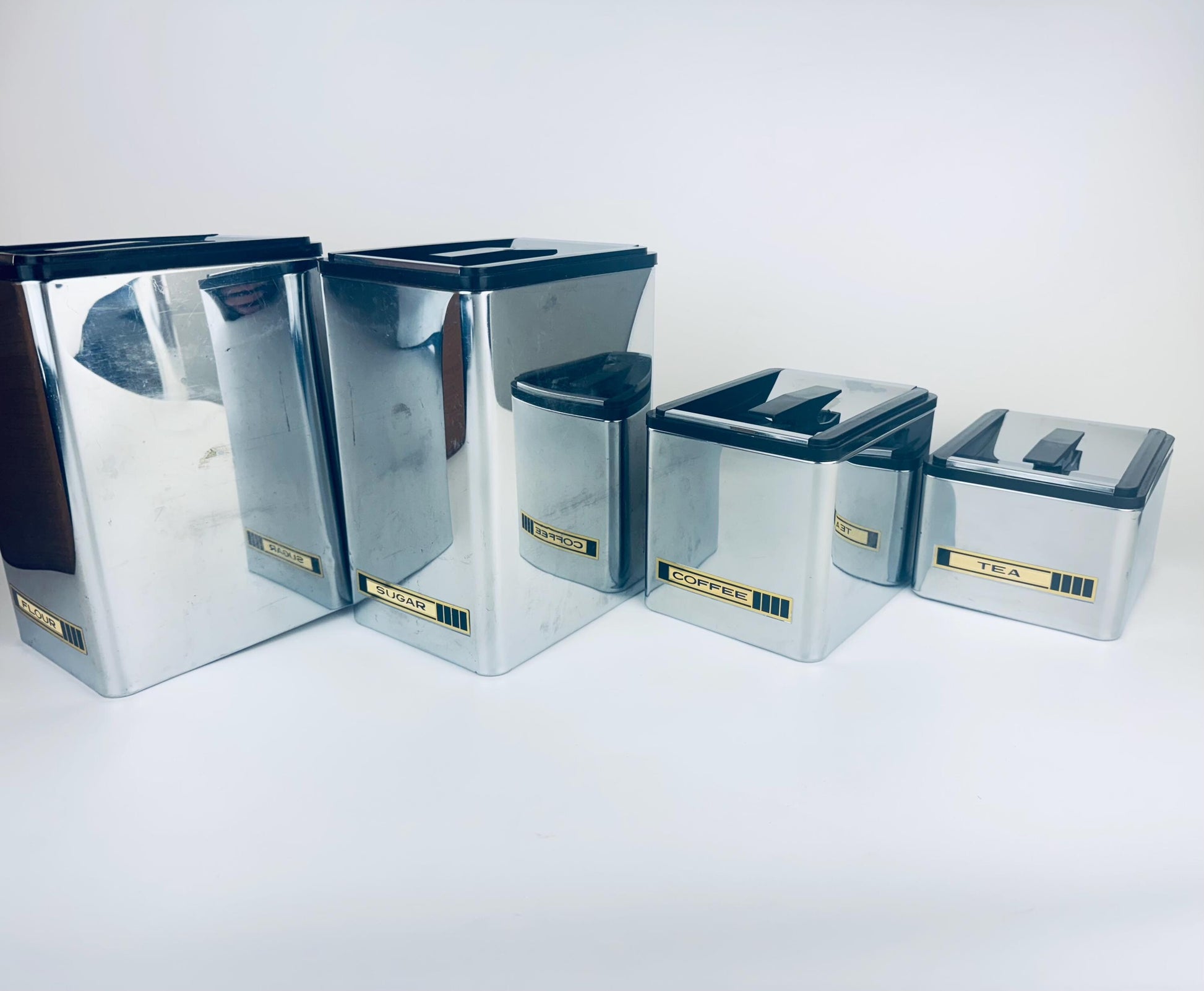 Set of silver canisters with black lids on a white background