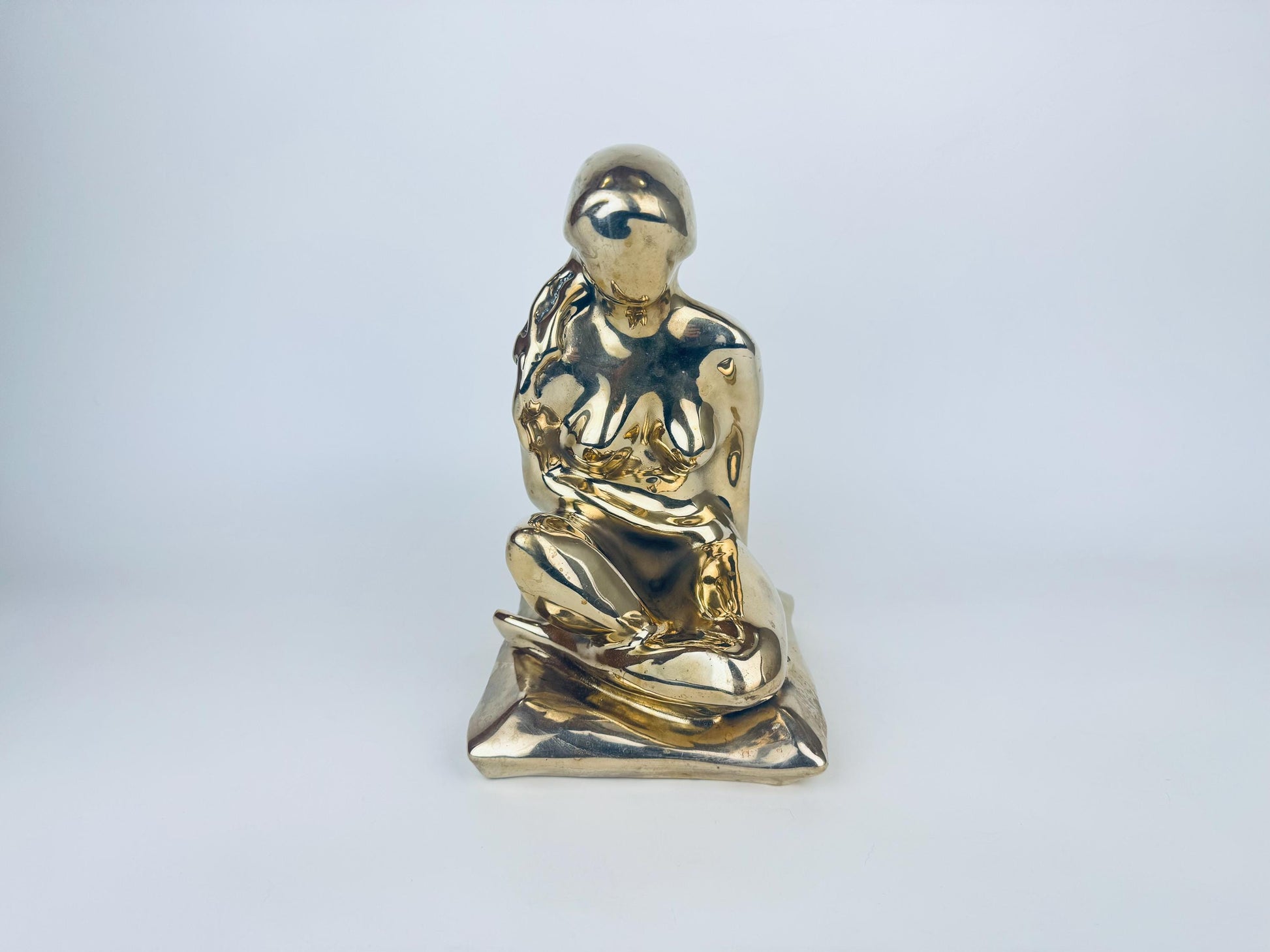 Gold-colored sculpture of a seated figure on a light gray background