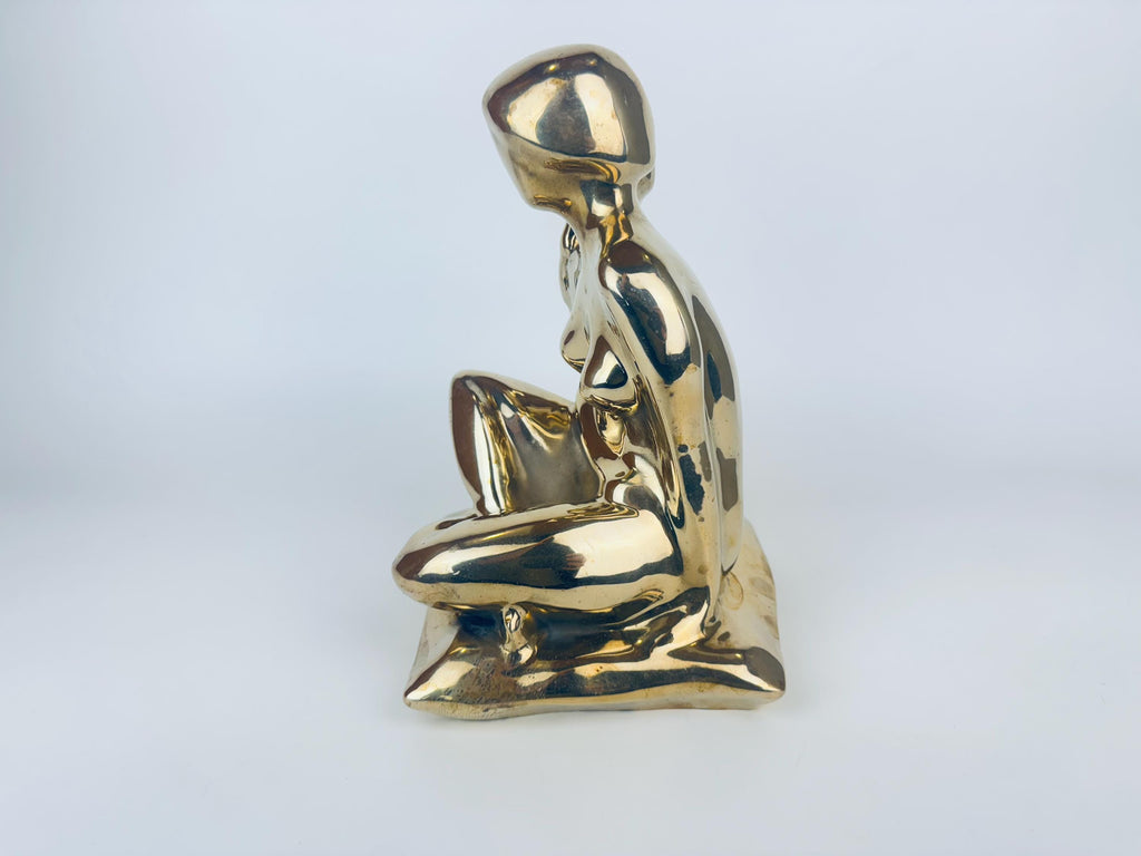 Gold sculpture of a seated figure on a light gray background
