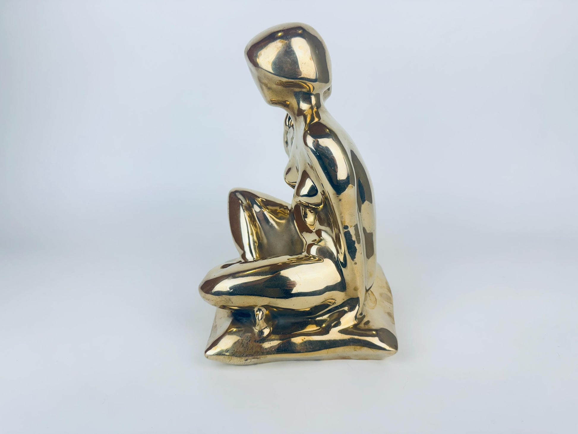 Gold sculpture of a seated figure on a light gray background