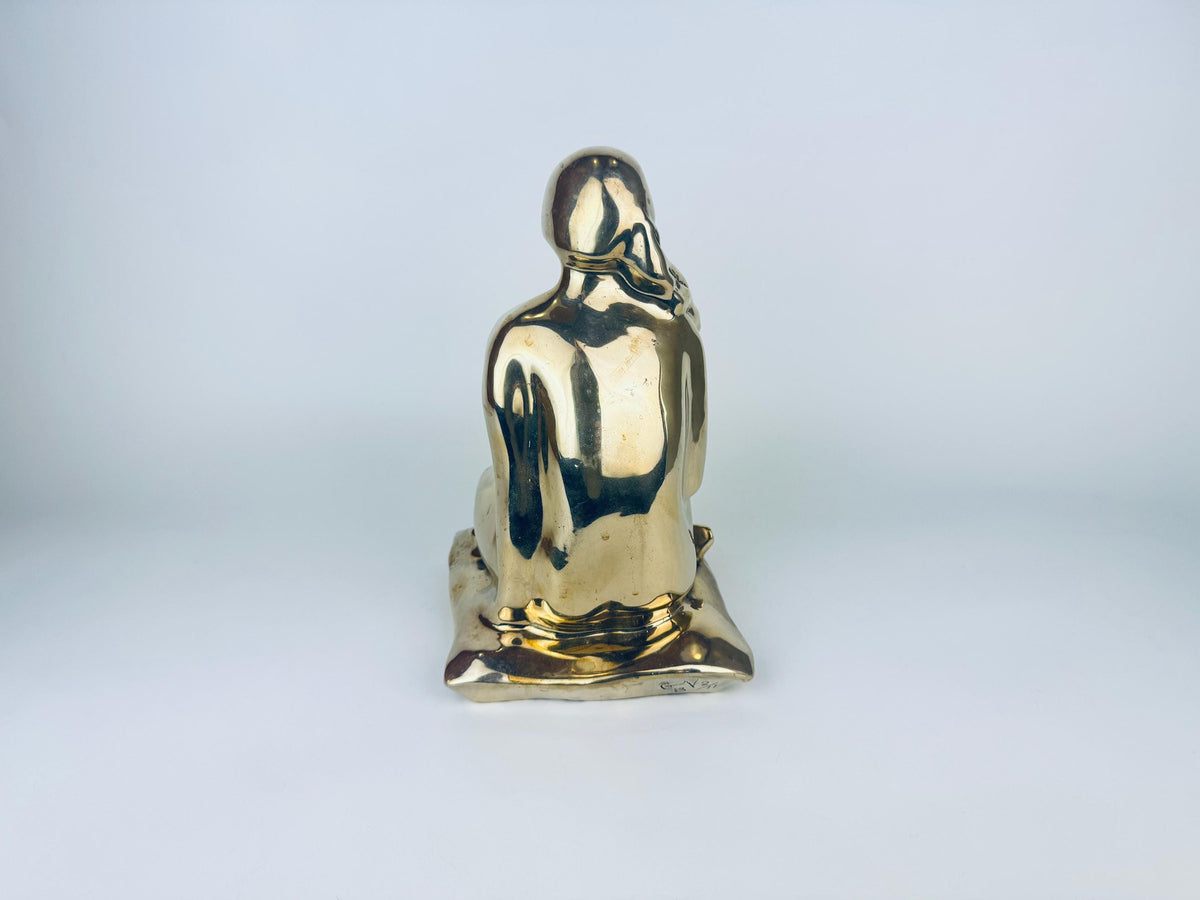 Gold-colored statue of a seated figure on a light gray background