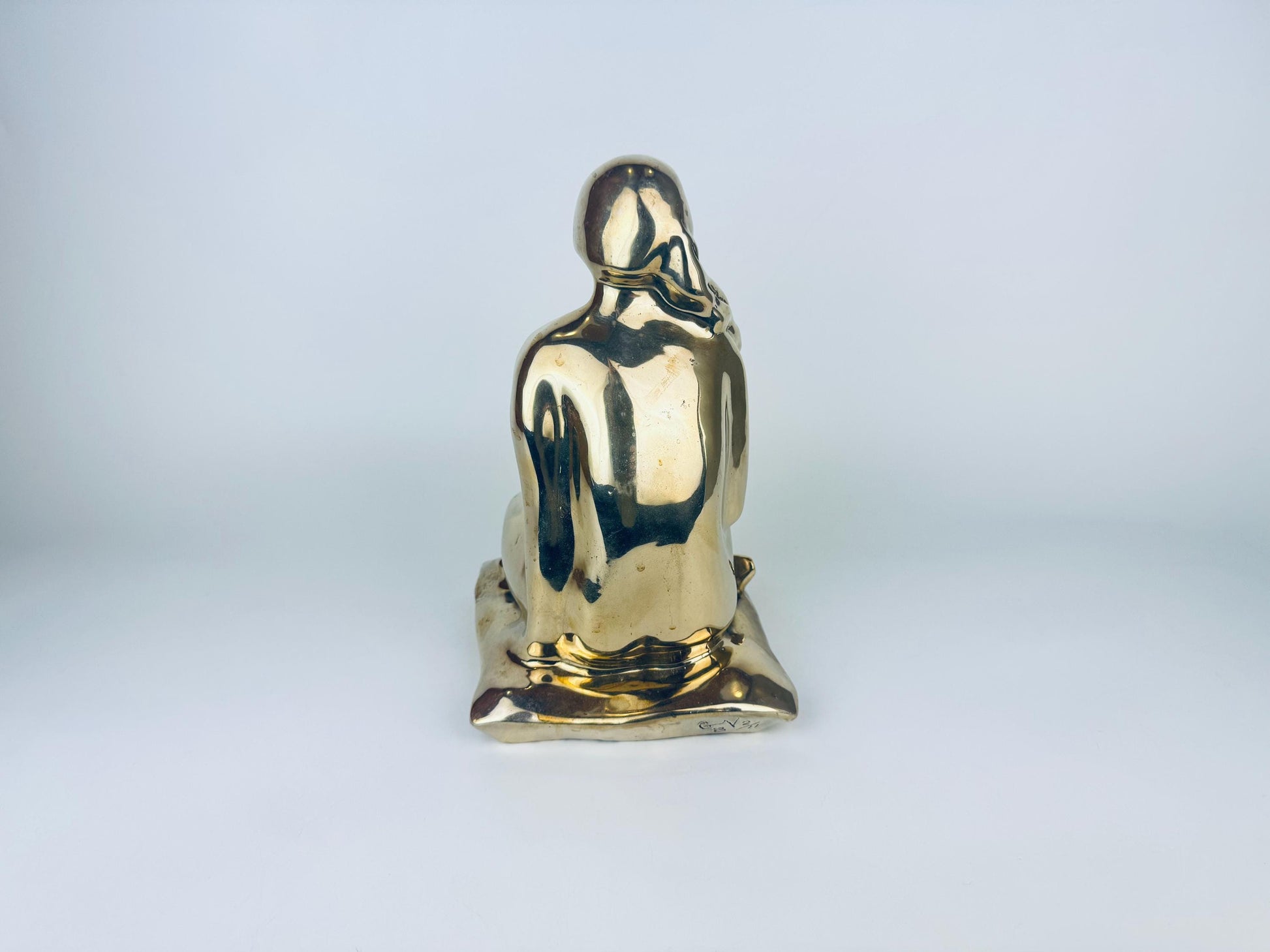 Gold-colored statue of a seated figure on a light gray background