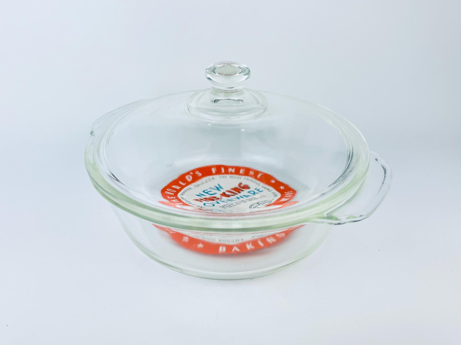 Glass baking dish with a lid featuring a brand logo on a white background