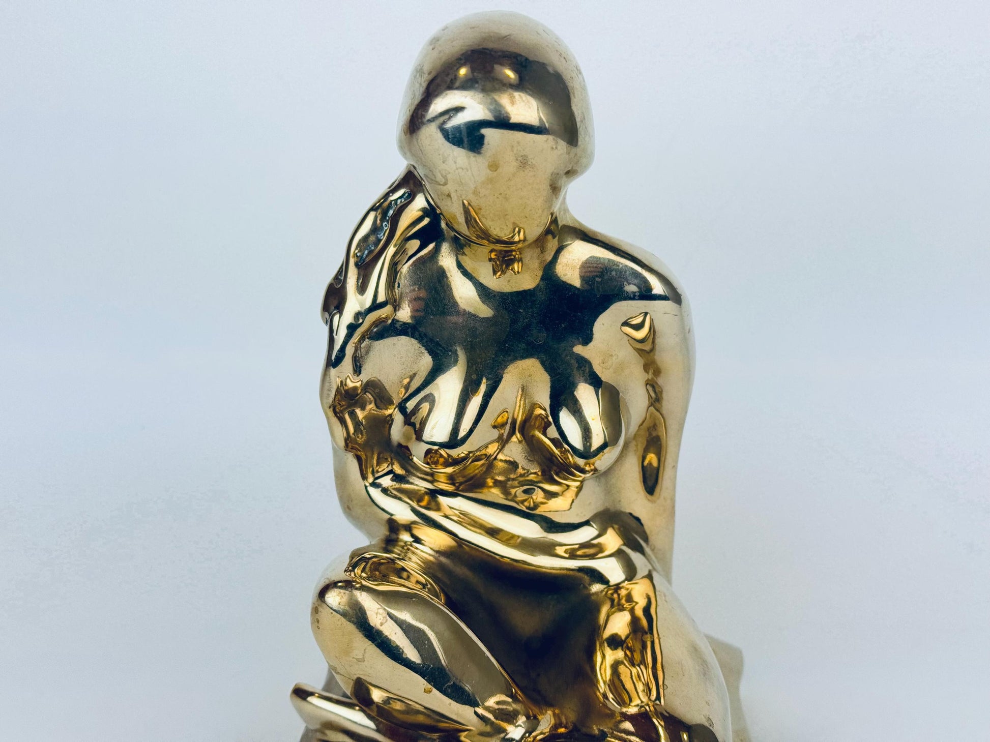 Gold sculpture of a nude figure on a light gray background