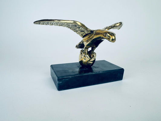 Brass eagle sculpture on a black swirl marble base against a white background