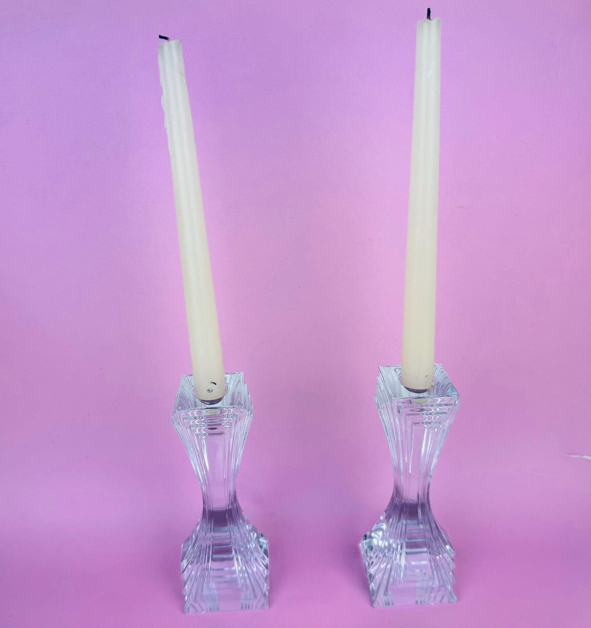 Two crystal candle holders with white candles on a pink background