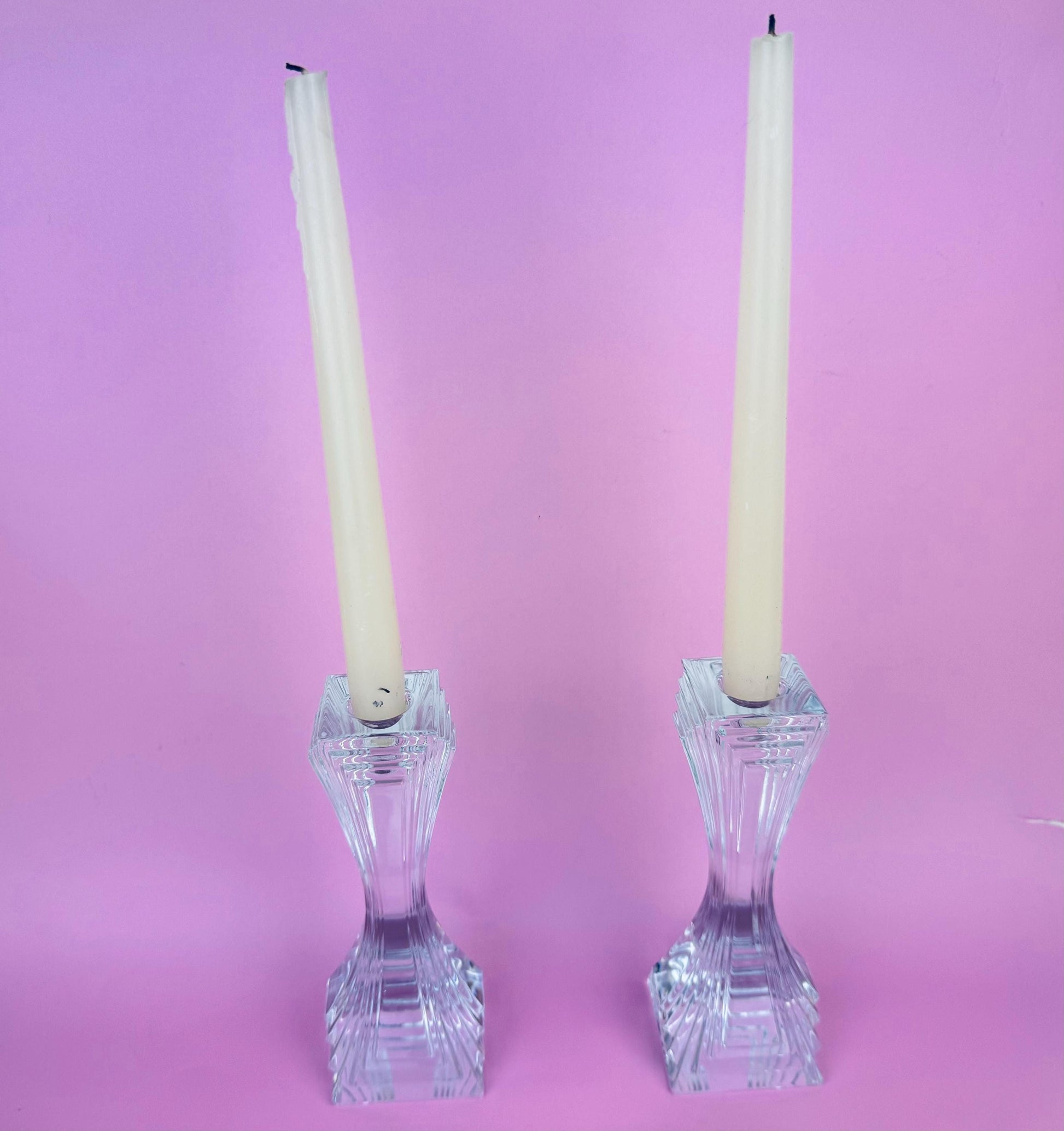 Two crystal candle holders with white candles on a pink background