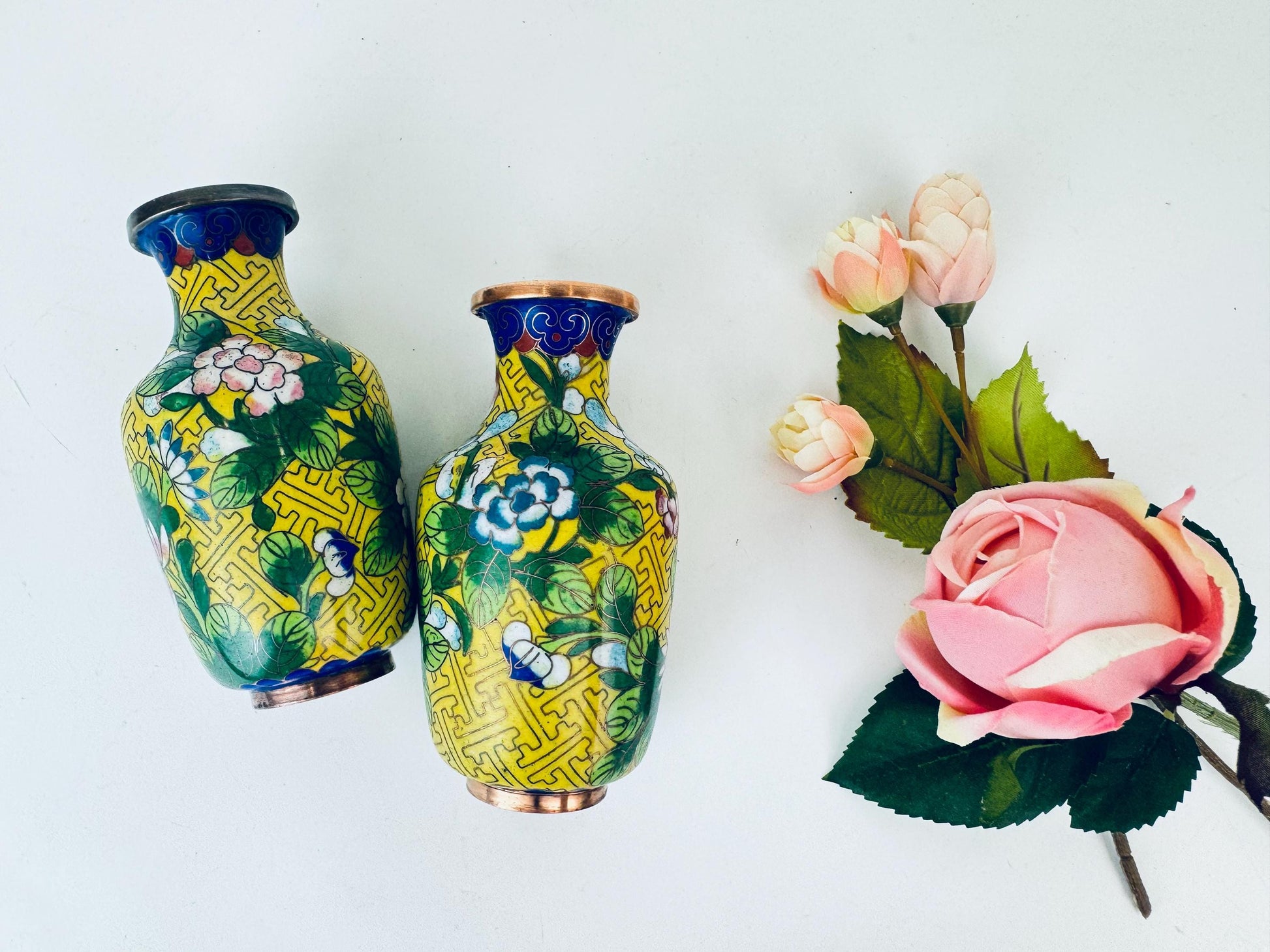 Two decorative vases with floral patterns on a white background, accompanied by a small bouquet of pink flowers.