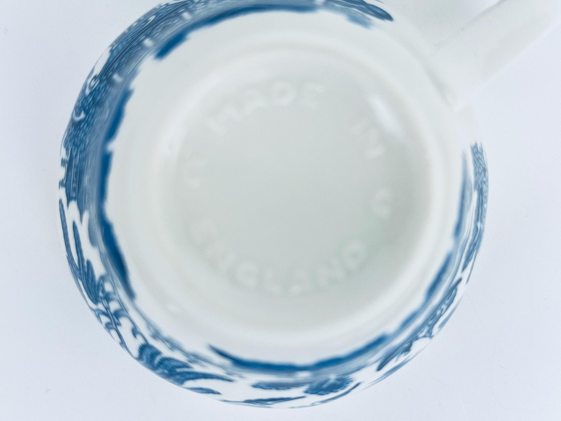 Close-up of a ceramic mug bottom with blue decorative rim on a white background