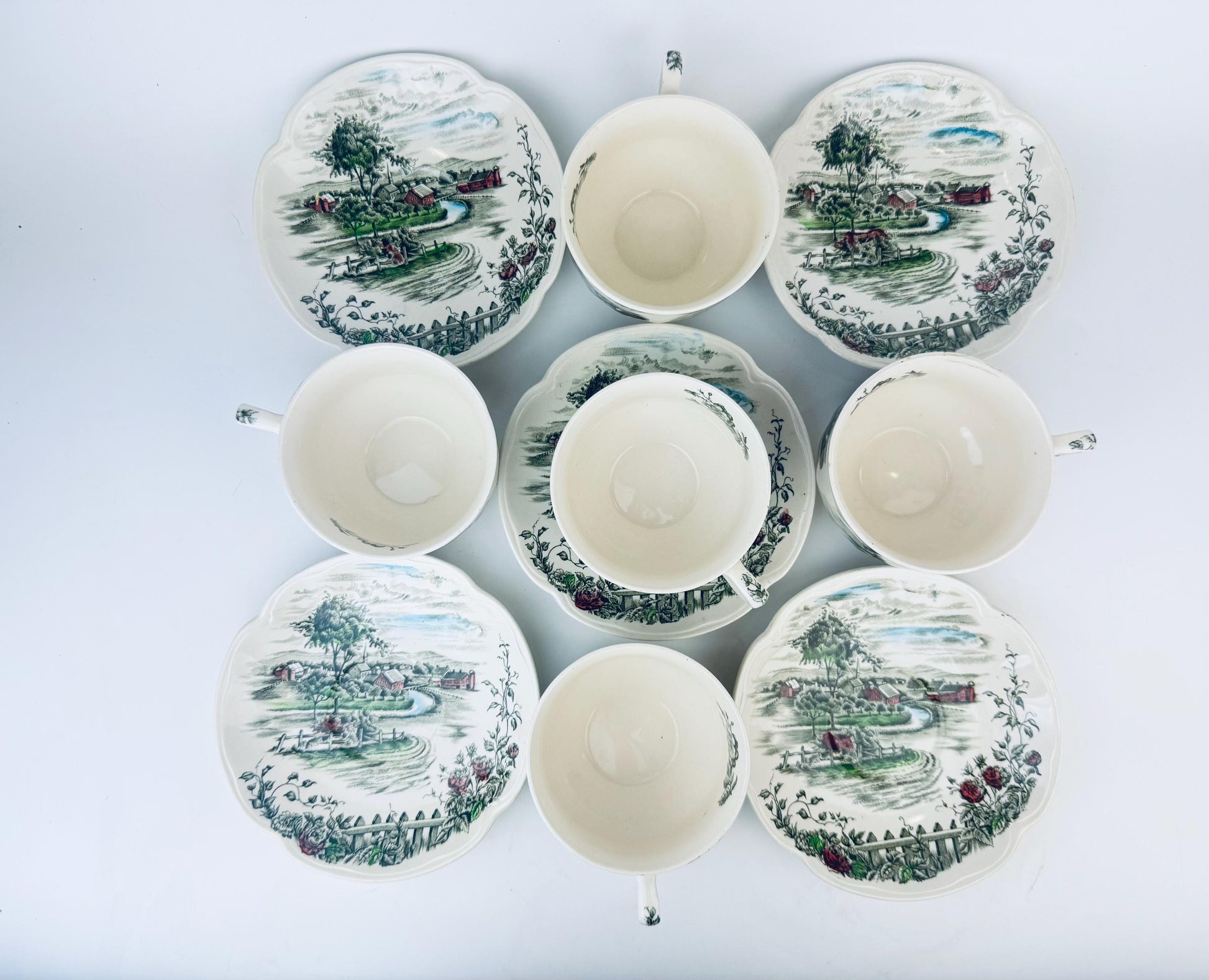 Set of ceramic teacups and saucers with scenic designs on a white background