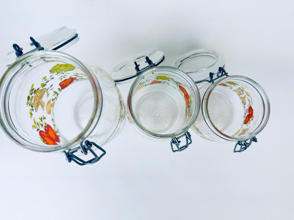 Set of three glass jars with floral lids on a white background