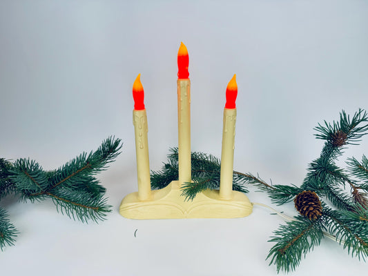 Decorative candle holder with three candles on a white background with greenery