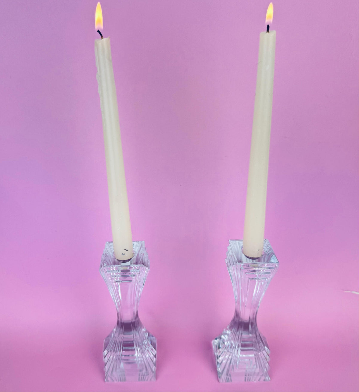 Two crystal candlesticks with lit candles on a pink background