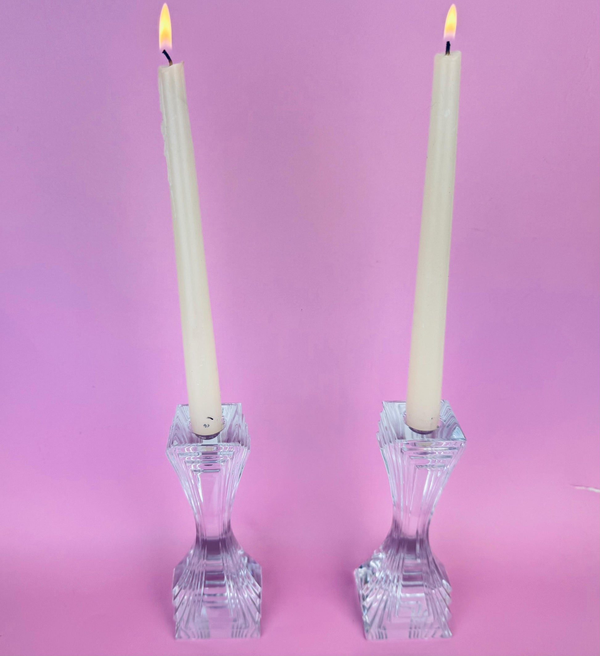 Two crystal candlesticks with lit candles on a pink background