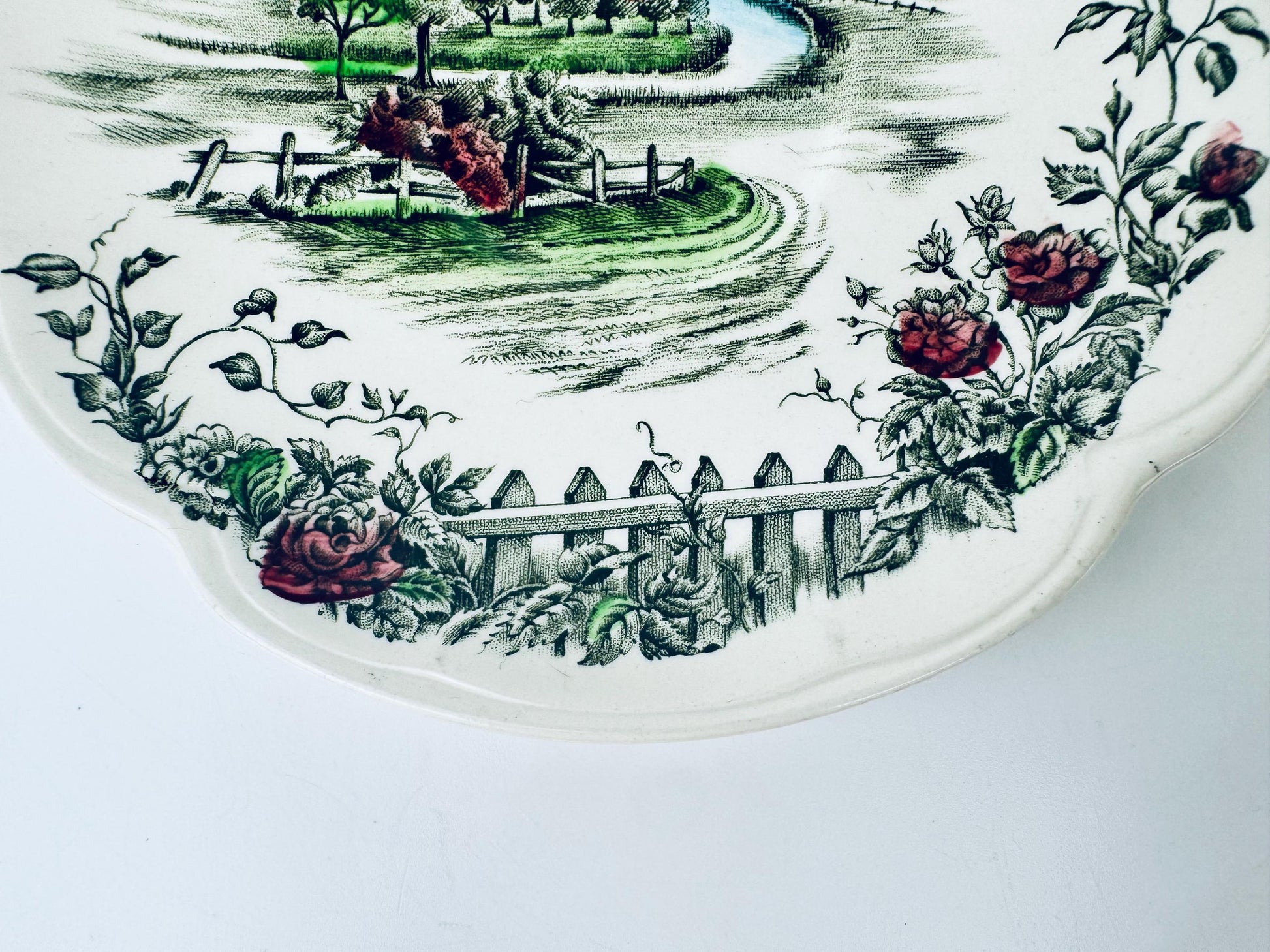 Decorative saucer plate with garden scene and roses on a white background
