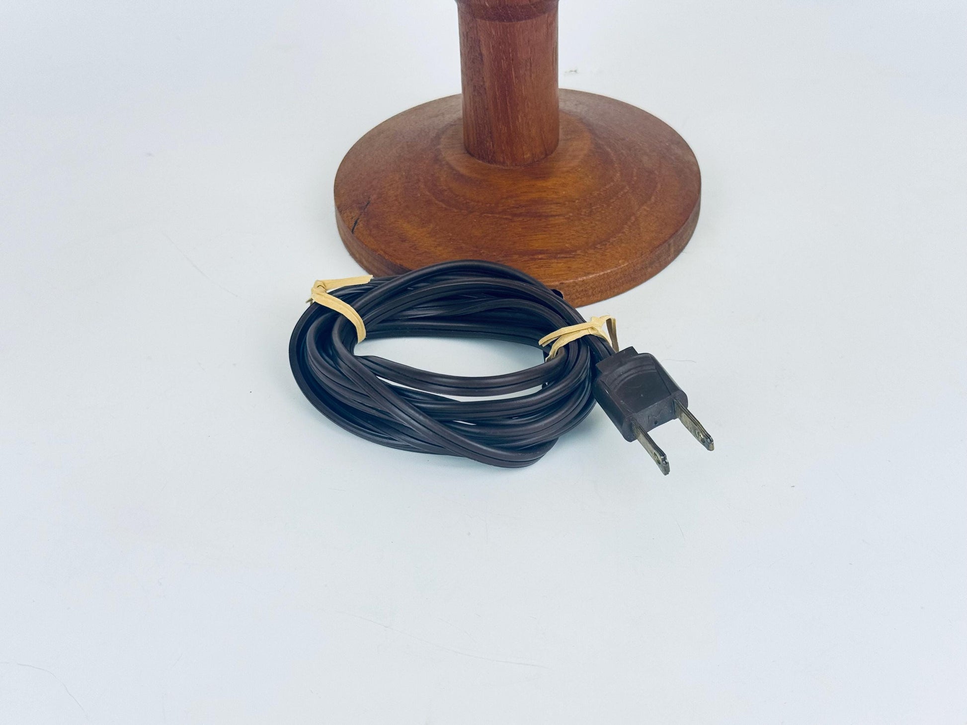 Wooden lamp base with black electrical cord and plug on a white background