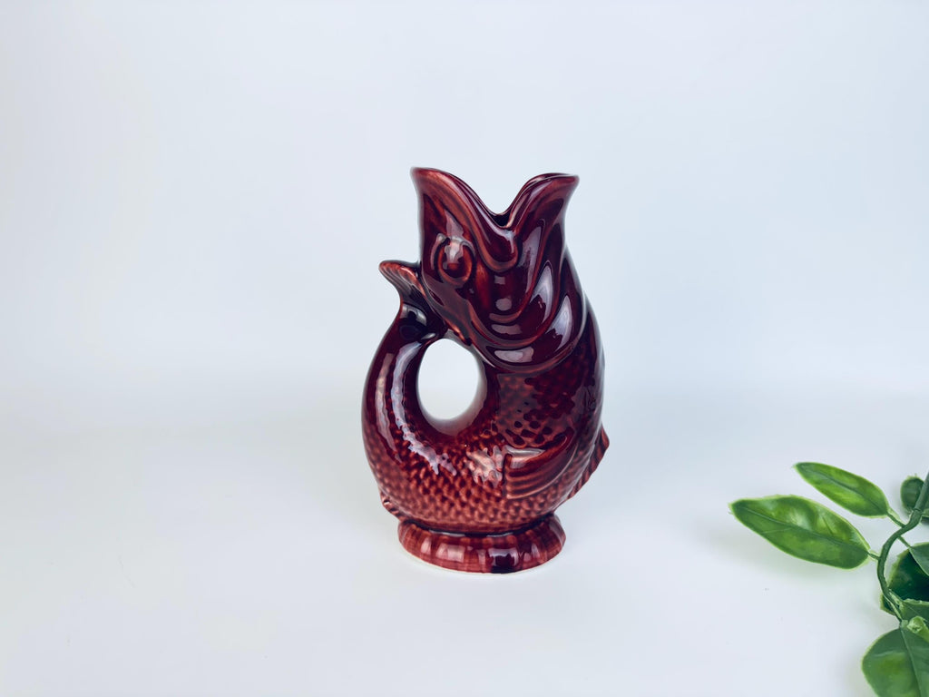 Vintage ceramic fish-shaped pitcher vase in glossy deep red glaze with leafy accent beside it