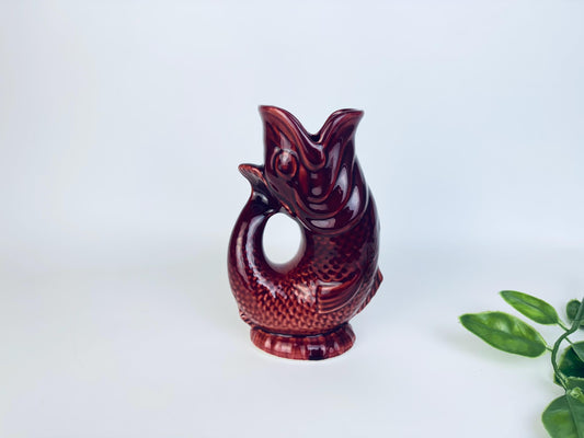 Vintage ceramic fish-shaped pitcher vase in glossy deep red glaze with leafy accent beside it