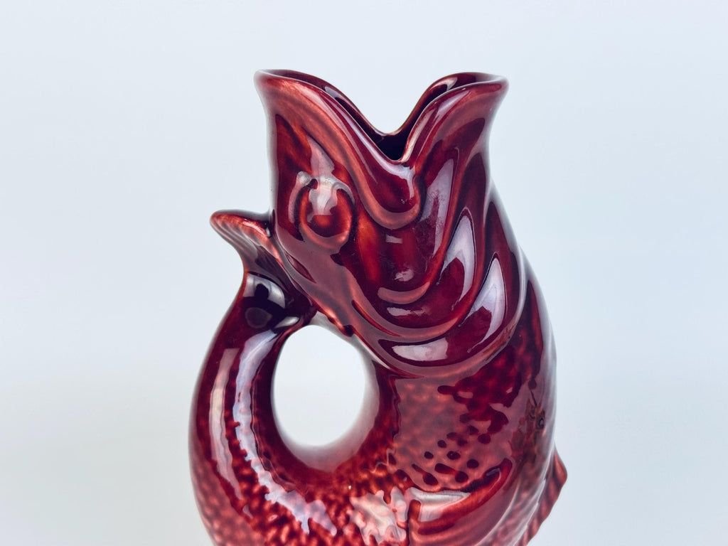 Side angle of vintage red ceramic fish pitcher showing curved tail and circular opening design