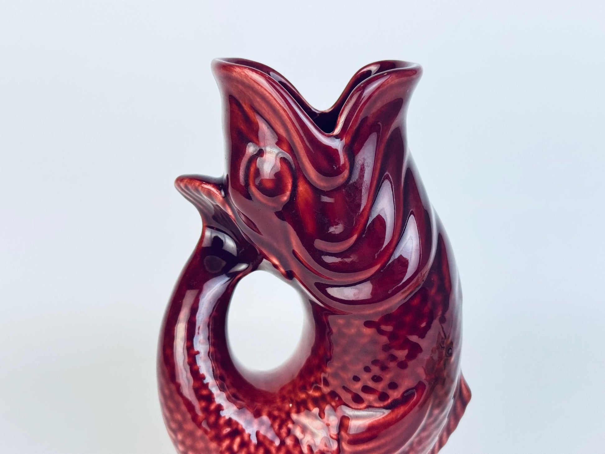 Side angle of vintage red ceramic fish pitcher showing curved tail and circular opening design