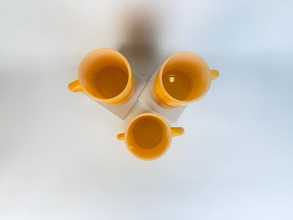 Three yellow cups stacked on a white surface with a light blue gradient background