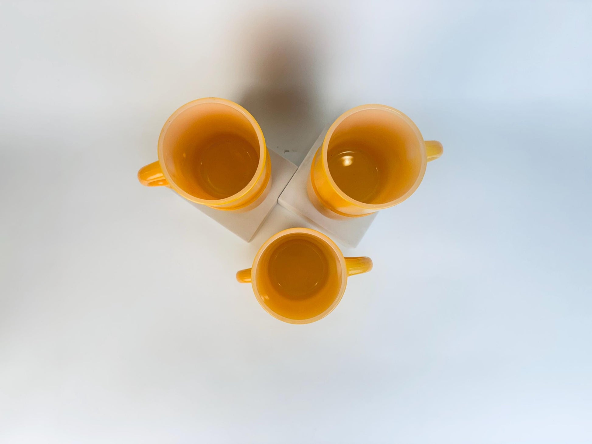 Three yellow cups stacked on a white surface with a light blue gradient background