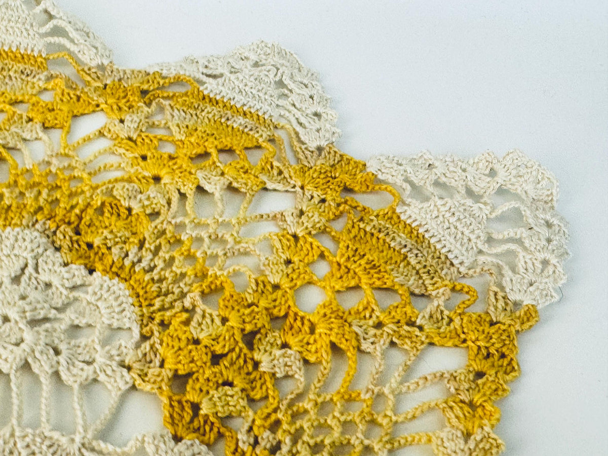 Macro detail of yellow and cream doily showing crochet joinery and texture