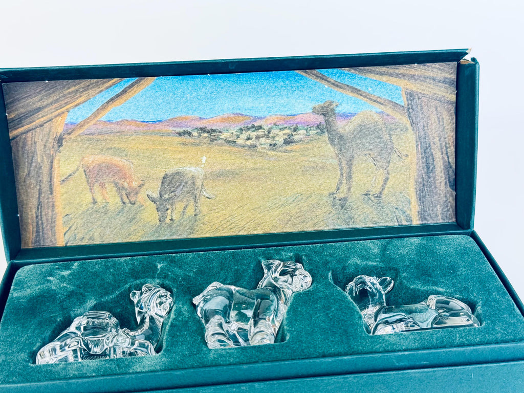 Close-up of Marquis by Waterford crystal nativity animals — cow, donkey, camel — resting in green velvet-lined presentation box.