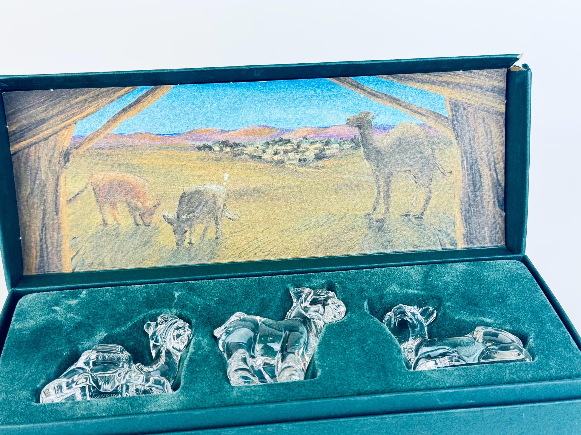 Close-up of Marquis by Waterford crystal nativity animals — cow, donkey, camel — resting in green velvet-lined presentation box.