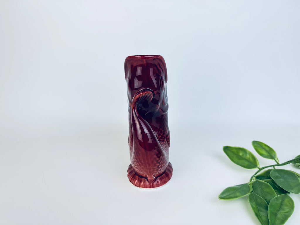 Tall side profile of fish-shaped pitcher in red ceramic glaze with greenery accent