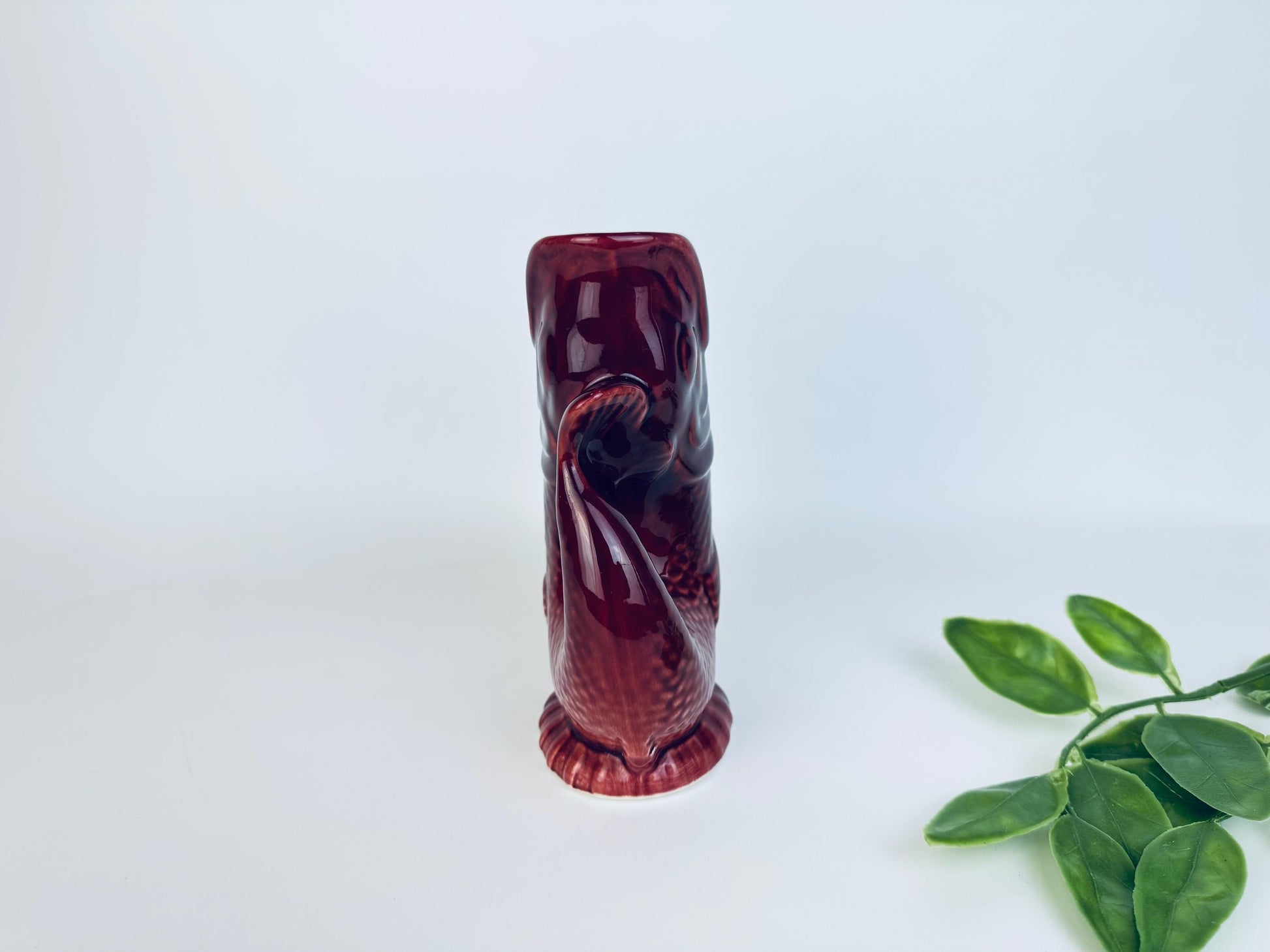 Tall side profile of fish-shaped pitcher in red ceramic glaze with greenery accent
