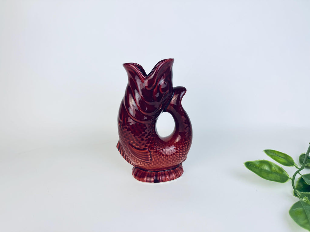 Full view of vintage red ceramic fish pitcher with plant leaves for scale reference