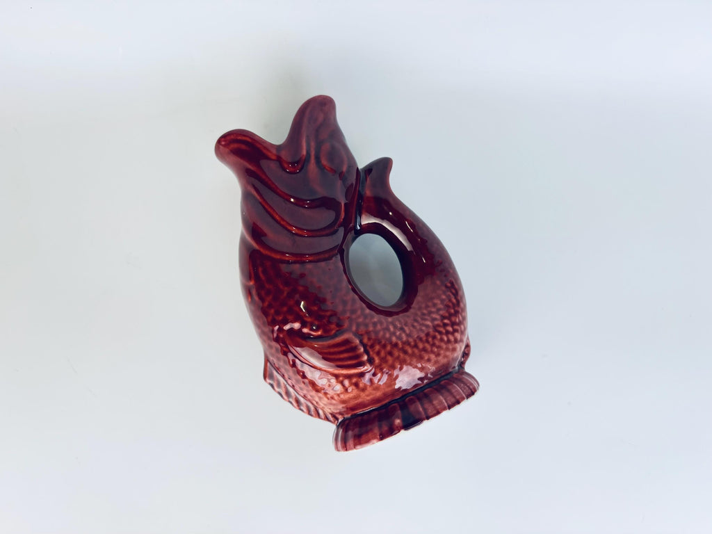 Overhead angled view of vintage red ceramic fish-shaped pitcher showing textured scales and glossy glaze finish