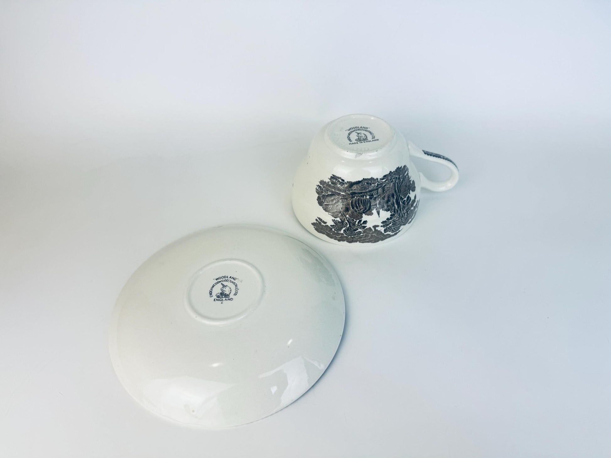 Vintage Woodland teacup and saucer by Enoch Wedgwood shown upside down to display backstamps, black transferware floral pattern visible on cup