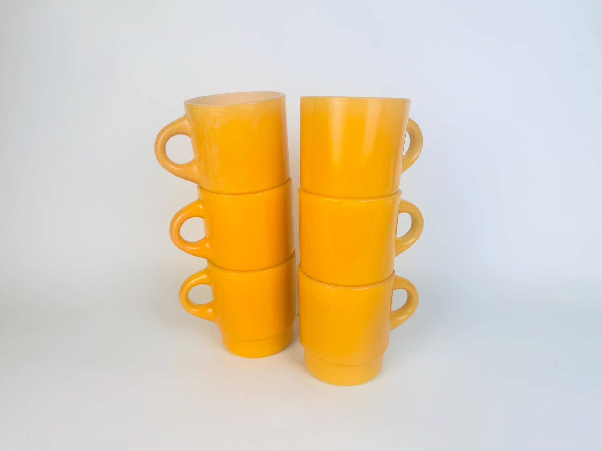 Set of yellow ceramic mugs stacked on a white background
