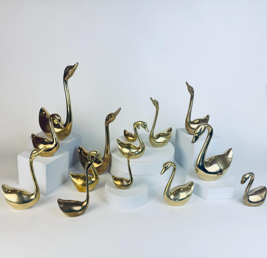 Gold swan sculptures on white pedestals against a light gray background
