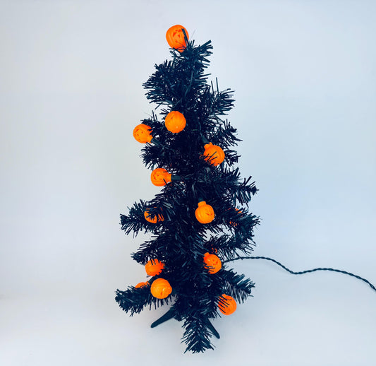 Small black tabletop tree decorated with vintage orange pumpkin jack-o’-lantern string lights, resembling twinkling bulbs, displayed on a white background.