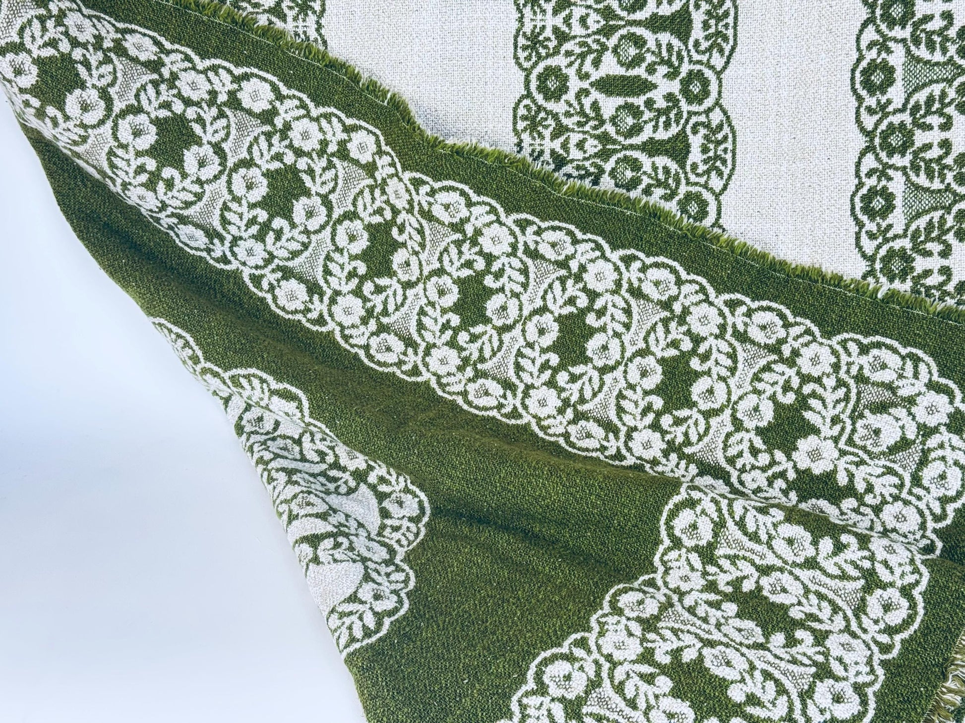 Close-up of green fabric with white lace trim on a white background