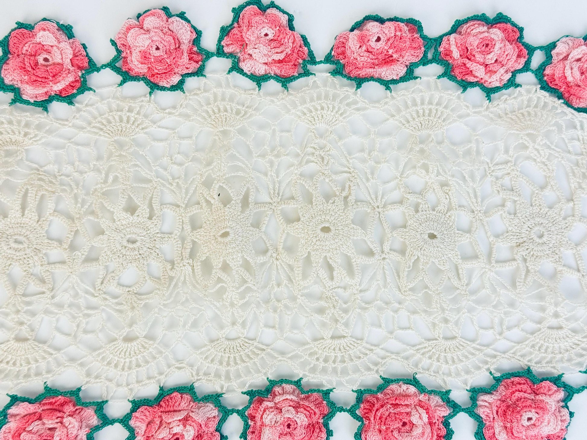 Close-up of pink crocheted roses and green leaves on lace border