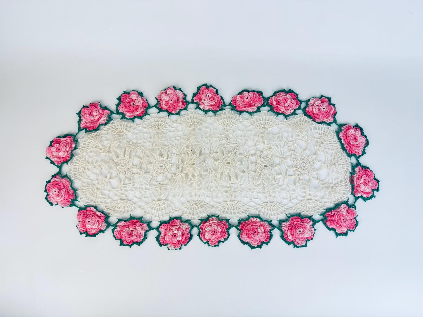 Overhead view of vintage crocheted table runner with pink rose border on white background