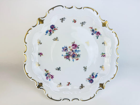 Decorative ceramic cake stand plate with floral patterns and gold trim on a white background.