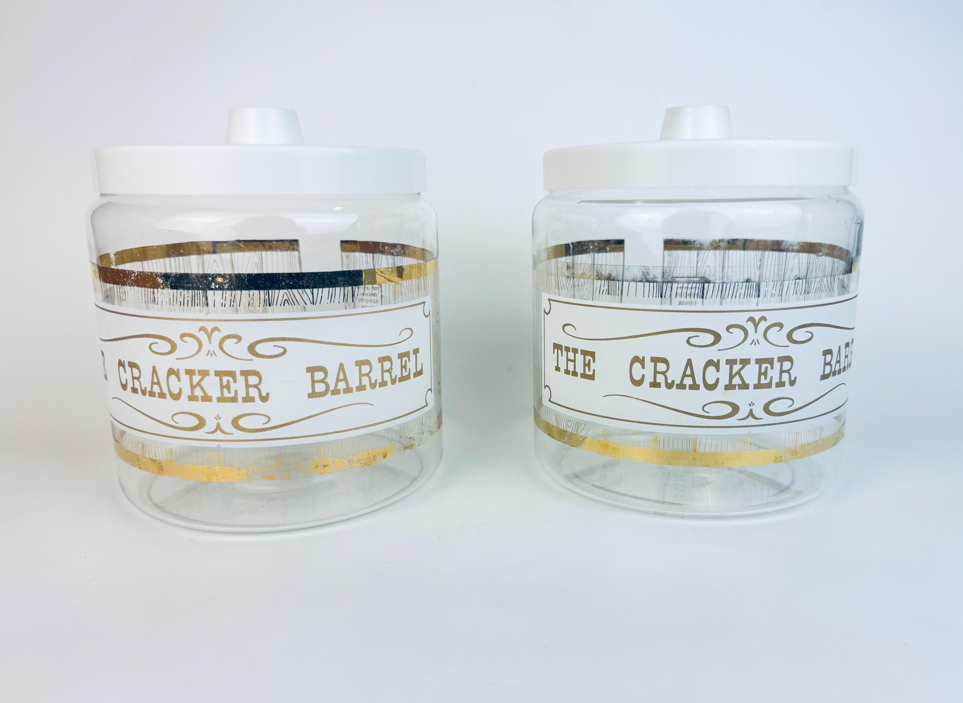 Pair of vintage Pyrex Cracker Barrel glass jars with white lids and gold decal design.