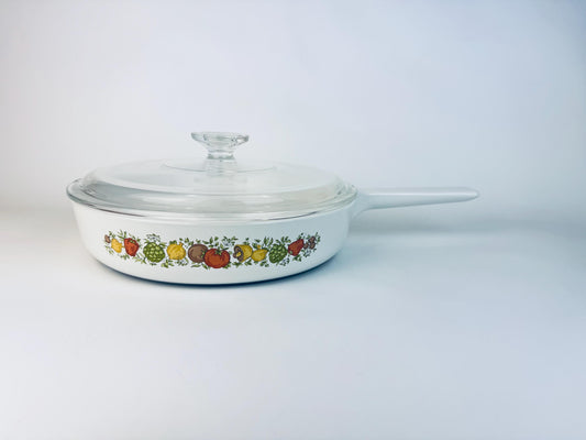 Vintage CorningWare skillet with glass lid featuring the Spice of Life pattern, decorated with colourful illustrations of vegetables and herbs on white Pyroceram cookware.